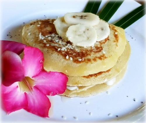 a plate with a stack of pancakes with bananas and a flower at Mango Moon in Pemuteran