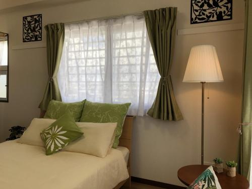 a bed with green and white pillows and a window at TerraceRin YN31 in Tomigusuku