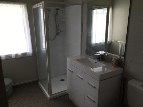 a white bathroom with a shower and a sink at Sapphire Springs Holiday Park and Thermal Pools in Katikati