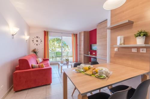 a living room with a table and a red chair at Résidence Hôtelière Natureva & Spa in Cap d'Agde