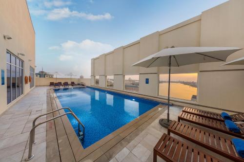 a swimming pool with benches and an umbrella at Citymax Hotel Ras Al Khaimah in Ras al Khaimah