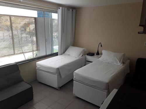2 camas en una habitación con ventana y sofá en Studio 208 - Perto UNB en Brasilia