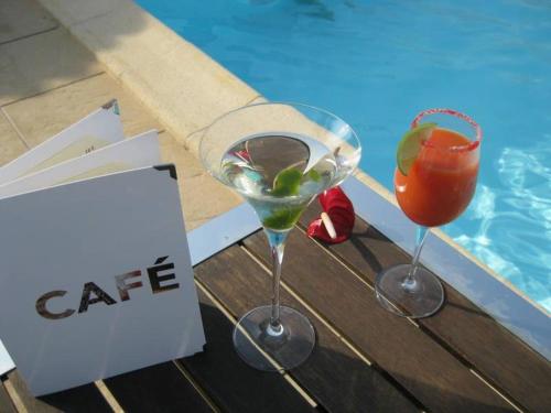 dos copas de vino sentadas en una mesa junto a una piscina en Locations de Vacances Le Clos Rhea, en Saint-Martin-de-Ré