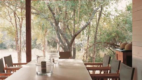 una mesa con sillas y una gran ventana con árboles en Hideaways Lazuli Bush Lodge, Hluhluwe, en Hluhluwe