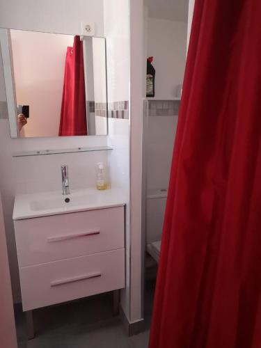 La salle de bains est pourvue d'un lavabo et d'un rideau de douche rouge. dans l'établissement Naturist Paradise in « Swinging Cap », au Cap d'Agde