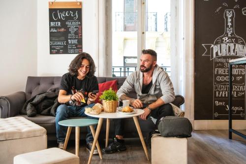 two men sitting on a couch in a living room at Safestay Madrid Central in Madrid