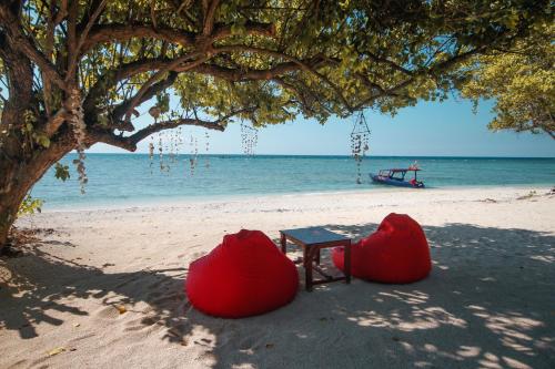 a table and chairs under a tree on a beach at Mimpi Bungalow in Gili Meno