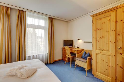 Cette chambre comprend un lit, un bureau et une fenêtre. dans l'établissement Hotel Meierhof, à Davos