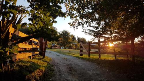 a dirt road next to a fence with the sun setting at Turismo Jaos Cabañas Tinas y Quincho in Futrono
