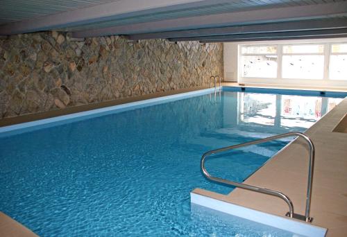 a swimming pool with blue water and a stone wall at Monami Apartments Klosters, Apt. Solavers No 1 in Klosters