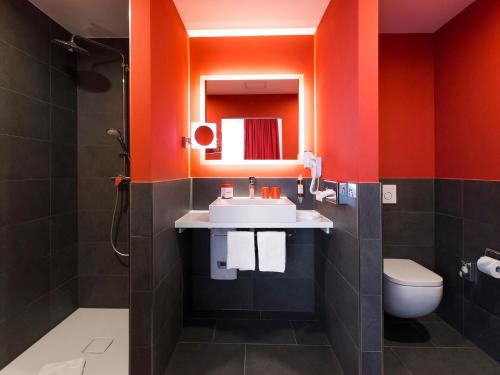 ein orangefarbenes Badezimmer mit einem Waschbecken und einem WC in der Unterkunft DORMERO Hotel Roth in Roth