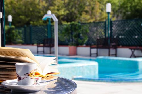 a coffee cup and book on a table next to a pool at Hotel Gaby in Rimini