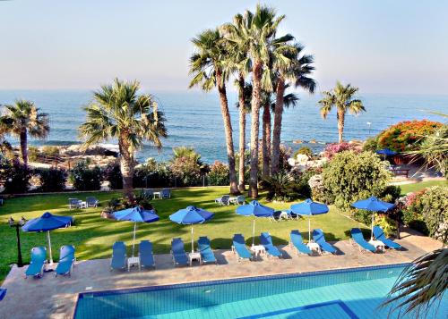 a pool with chairs and umbrellas and the ocean at Rododafni Beach Apartments in Paphos City