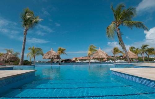 a swimming pool with palm trees and umbrellas at Spanish Water View Apartments - Jan Thiel area in Willemstad