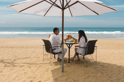 Amal Beach Hotel في بينتوتا: يجلس شخصان على طاولة تحت مظلة على الشاطئ