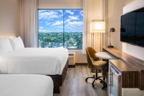 a hotel room with a bed and a desk and a window at Wyndham Garden Ft Lauderdale Airport & Cruise Port in Dania Beach