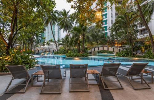 a pool with chairs and tables in front of a building at Chatrium Sathon Bangkok in Bangkok