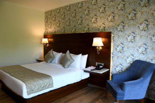 a bedroom with a bed and a blue chair at Mastiff Villa Camellia by OTHPL in Pālampur