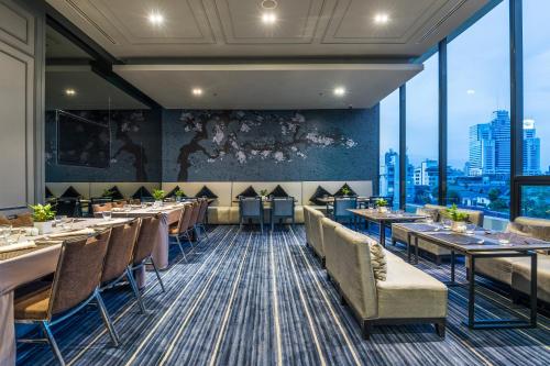 a dining room with tables and chairs and large windows at Chatrium Sathon Bangkok in Bangkok