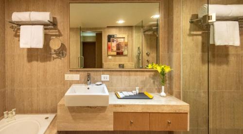 a bathroom with a sink and a mirror and a tub at Radisson Gurugram Sohna Road City Center in Gurgaon