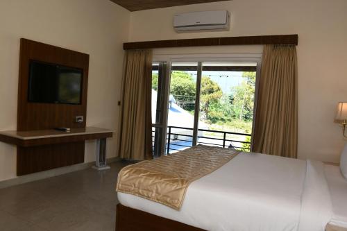 a bedroom with a bed and a television and a balcony at Mastiff Villa Camellia by OTHPL in Pālampur