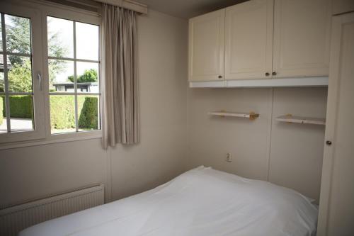 a white bedroom with a bed and a window at Heuveltjes 4 pers. bungalow in Voorthuizen