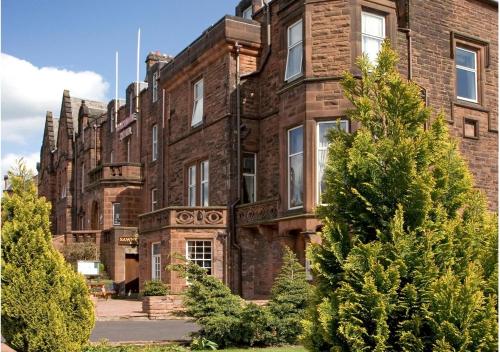 an old brick building with trees in front of it at Cairndale Hotel & Spa in Dumfries