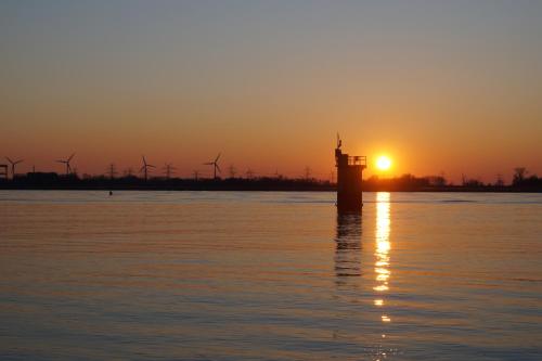 a lighthouse in the water at sunset with windmills at FeWo Düver in Loxstedt