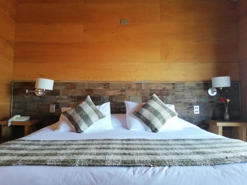 a bedroom with a white bed with pillows and a wooden wall at Hotel Parque Quilquico in Castro
