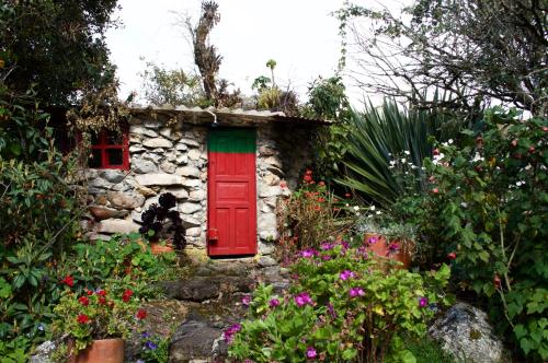 una pequeña casa de piedra con una puerta roja y flores en Casa de piedra El Colibrí en Guasca