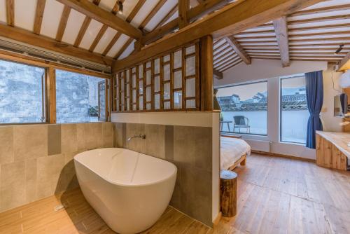 a bathroom with a tub and a bed and windows at Huangshan Xidi Shang De Tang in Yi