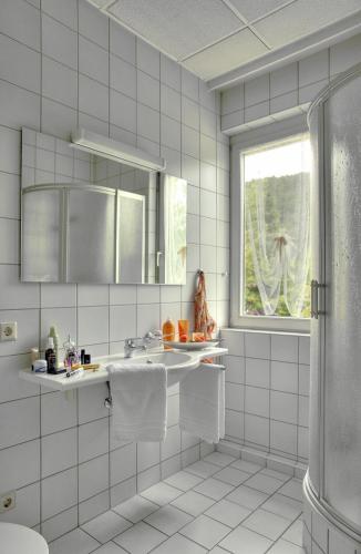 a white tiled bathroom with a sink and a window at Hotel Teinachtal in Bad Teinach-Zavelstein