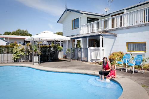 uma mulher e uma criança sentados à beira de uma piscina em Accommodation at Te Puna Motel em Tauranga