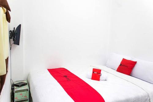 RedDoorz @ Galuh Mas في كراوانغ: سرير أبيض مع وسائد حمراء في الغرفة