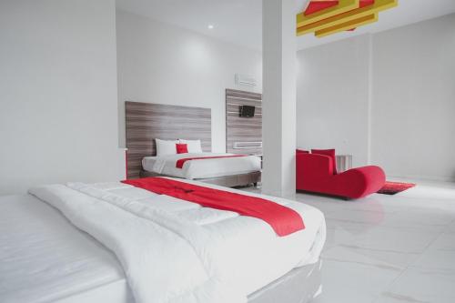 - une chambre blanche avec 2 lits et un fauteuil rouge dans l'établissement RedDoorz Syariah @ Jalan Dieng, à Wonosobo