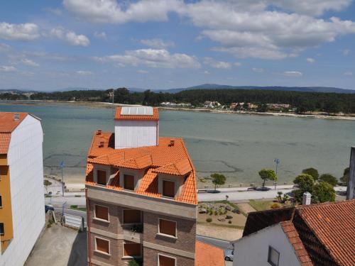 a building with an orange roof next to a body of water at Hostal Mourelos in O Grove