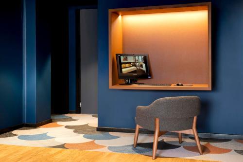 a room with a chair and a television on a blue wall at Hotel Le Bugatti in Molsheim