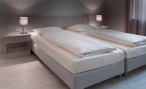 a bedroom with two beds with white sheets and lamps at Hotel Deutsches Theater in Munich