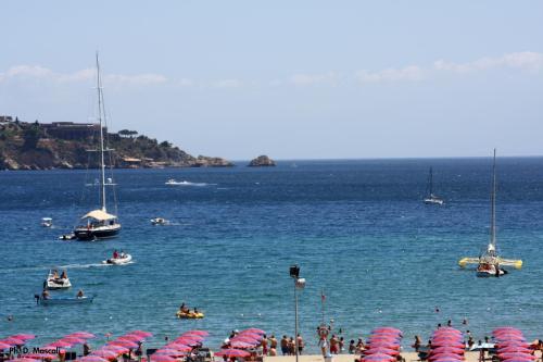 people on a beach with umbrellas and boats in the water at Porta del Vento in Giardini Naxos