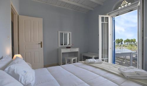 a white bedroom with a large bed and a large window at Nostos Beachfront Apartments & Studios in Agios Ioannis Tinos