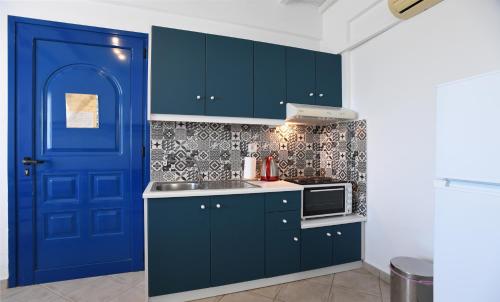 a kitchen with blue cabinets and a blue door at Nostos Beachfront Apartments & Studios in Agios Ioannis Tinos