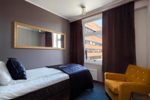 a room with a bed and a mirror and a chair at Grand Hotel Arendal - Unike Hoteller in Arendal