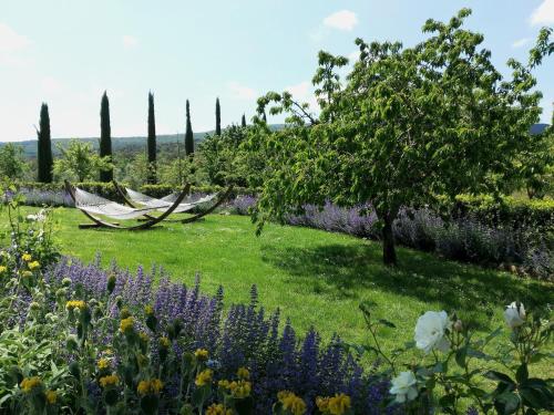 a garden with a tree and a hammock and flowers at Borgo dé Brandi in Monteriggioni
