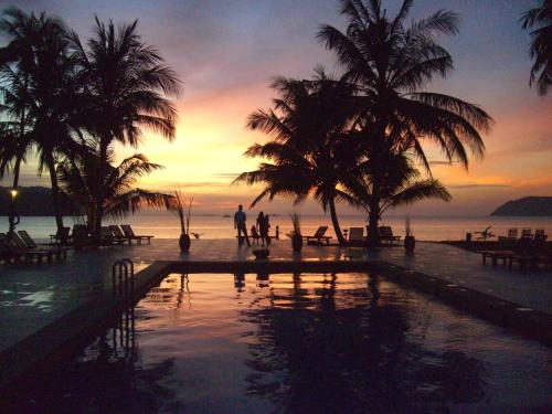 zwei Personen stehen in der Nähe eines Swimmingpools mit Palmen in der Unterkunft Frangipani Langkawi Resort in Pantai Cenang