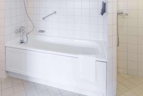 a white bath tub in a white tiled bathroom at Ramada by Wyndham Flensburg City in Flensburg
