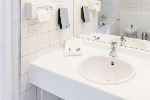 a white bathroom with a sink and a mirror at Ramada by Wyndham Flensburg City in Flensburg