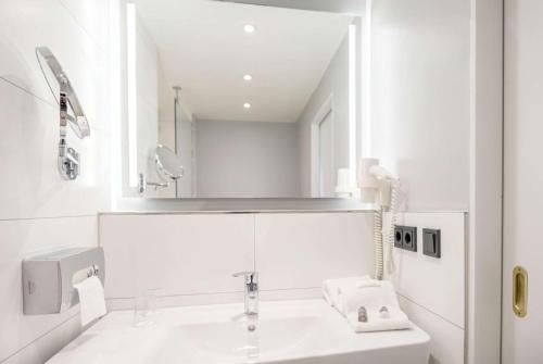 a white bathroom with a sink and a mirror at Ramada by Wyndham Flensburg City in Flensburg