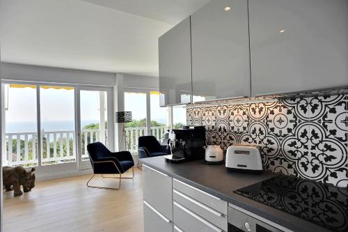 eine Küche mit einer Theke und einigen Stühlen und Fenstern in der Unterkunft Les Terrasses du parc Cordier in Trouville-sur-Mer