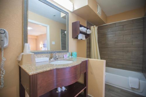 a bathroom with a sink and a mirror and a tub at The Crossroads Hotel and Suites Irving in Irving