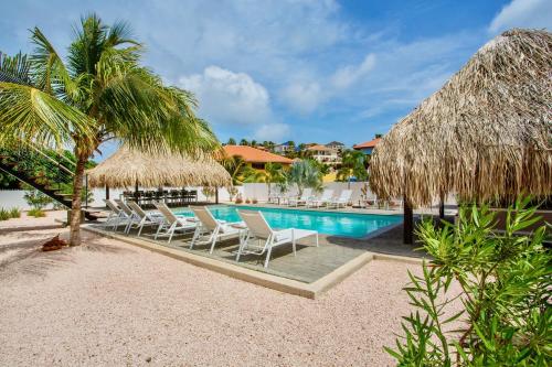 a resort pool with chairs and a straw umbrella at La Vista Luxury Apartment Jan Thiel in Jan Thiel